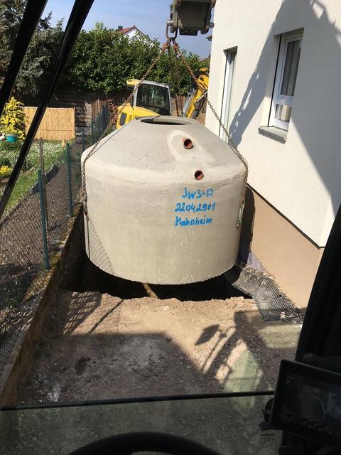 Betonzisterne wird per Kran in die ausgehobene Grube neben einem Haus gehoben